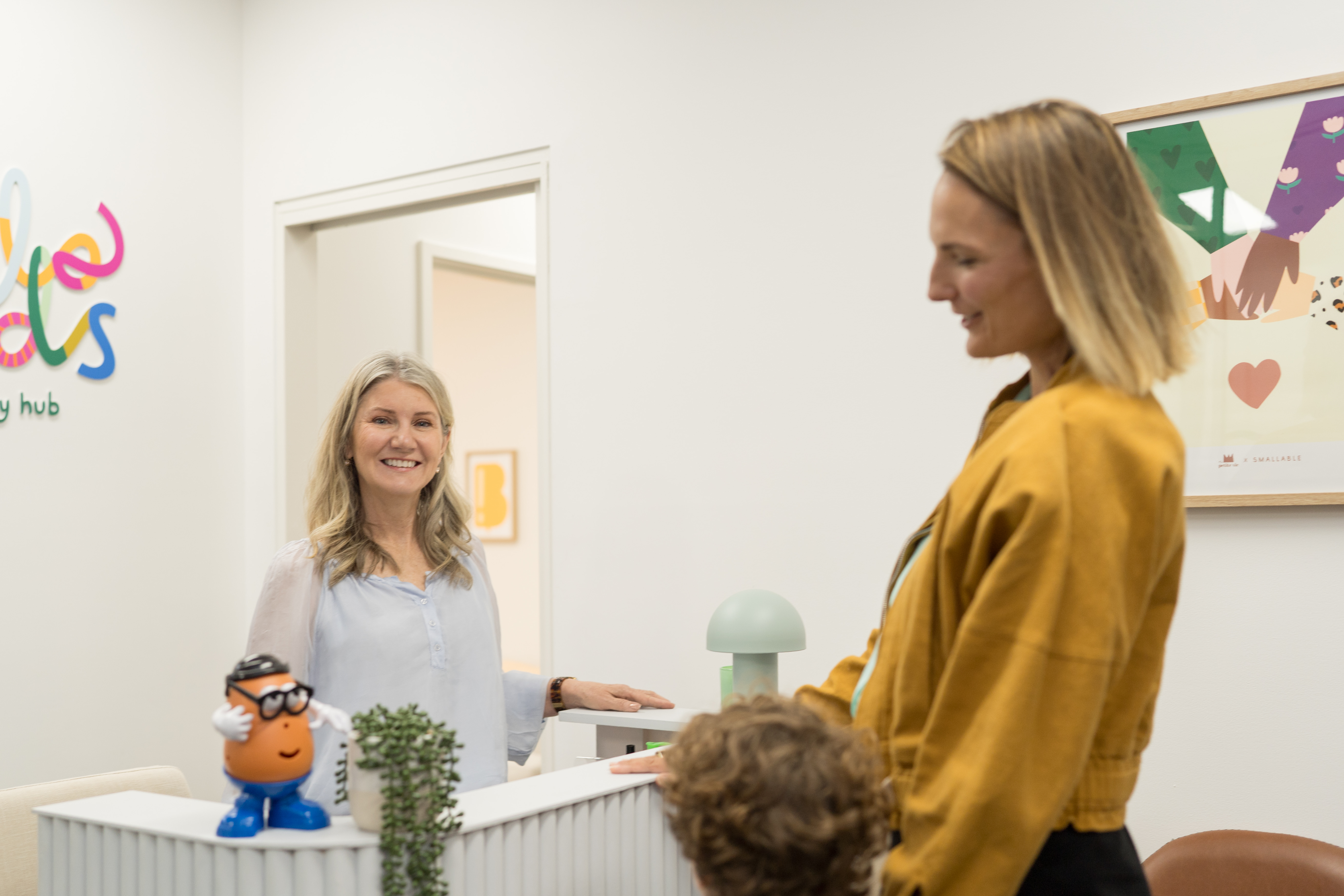 An educator warmly welcoming a parent and young child into the Hello Kids clinic